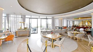 Een ruim restaurant met ronde tafels en stoelen, een centraal gelegen bar en grote ramen voor natuurlijk licht.