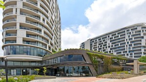 Een modern hotel met een gebogen gevel, een bushalte en een bordje met de tekst 'Luna Life Club'.