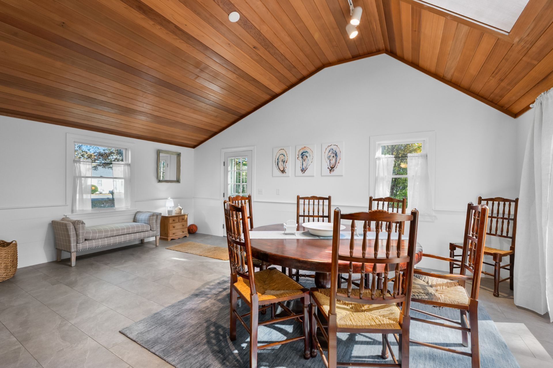 A spacious room with a high ceiling, a wooden dining table surrounded by chairs, a sofa, and a window with curtains.