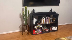 A living room with a flat-screen TV mounted on the wall, a black bookshelf with various items, a cactus plant, and a 'Wi-Fi' sign. - Private Room & Bath in Augusta (Augusta)