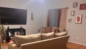 A living room with a beige sofa, a flat-screen TV, a bookshelf, and a ceiling fan. - Private Room & Bath in Augusta (Augusta)