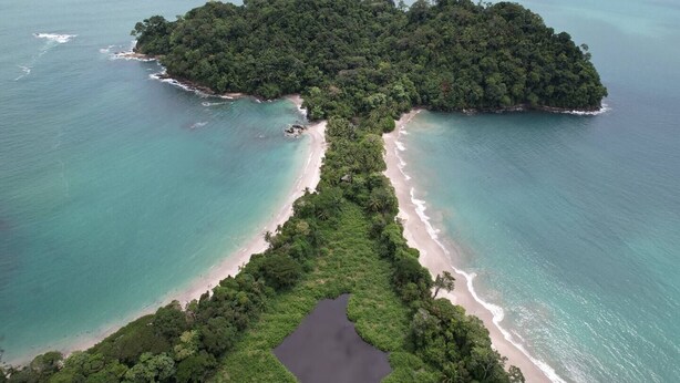 Luchtbeeld van een tropisch eiland met een smal strand, dicht bos en helder turquoise water.