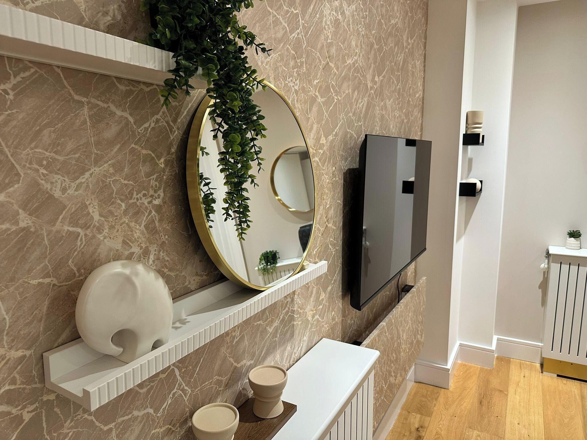 A modern bathroom with marble walls, a large mirror, a TV, and a white vanity.