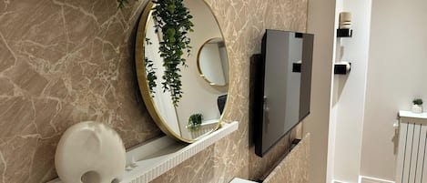 A modern bathroom with marble walls, a large mirror, a TV, and a white vanity.