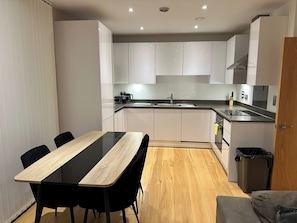 Eine moderne Küche mit weißen Schränken, einer schwarzen Arbeitsplatte, einem Spülbecken und einem Essbereich mit einem Holztisch und schwarzen Stühlen.
