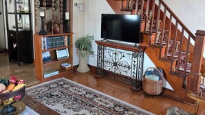 Een woonkamer met een houten trap, een flatscreen televisie, een boekenplank en een eettafel met placemat.