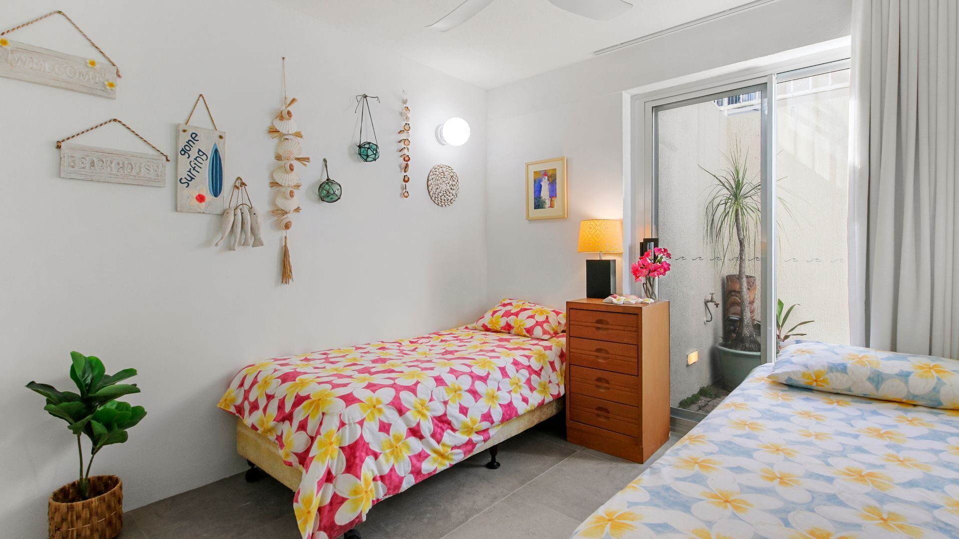 A bedroom with a bed, a dresser, a bedside table with a lamp, a wall-mounted light, and a window with curtains.