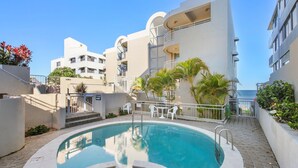 A modern building with a swimming pool, outdoor seating, and a view of the ocean. - Seaspray Unit 2, 21 Warne Tce, Kings Beach (Kings Beach)