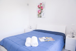 Ein ordentlich bezogenes Bett mit einer blauen Tagesdecke, zwei aufgerollte weiße Handtücher und eine Zeitschrift darauf.