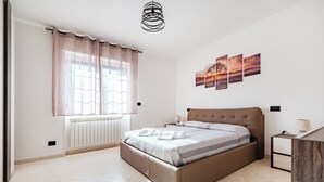 Ein Schlafzimmer mit Bett, Heizkörper, Fenster mit Vorhängen, Nachttisch und Wandbild.