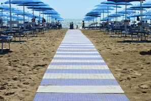 Uma praia com um tapete listrado que leva à água, guarda-sóis azuis e cadeiras de praia.