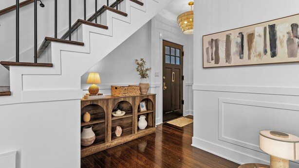 A staircase with wooden steps and black railings, a wooden console table with decorative items, a wall-mounted abstract painting, and a door with a glass panel.