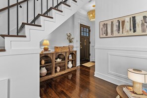 A staircase with wooden steps and black railings, a wooden console table with decorative items, a wall-mounted abstract painting, and a door with a glass panel.