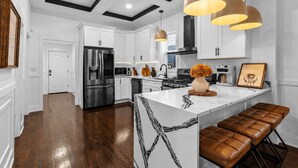A modern kitchen with white cabinetry, stainless steel appliances, and a central island with a marble countertop.