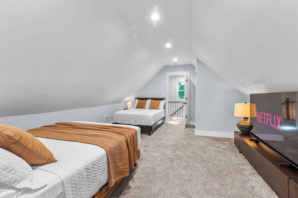 A bedroom with two beds, a TV, and a staircase leading to an upper level.