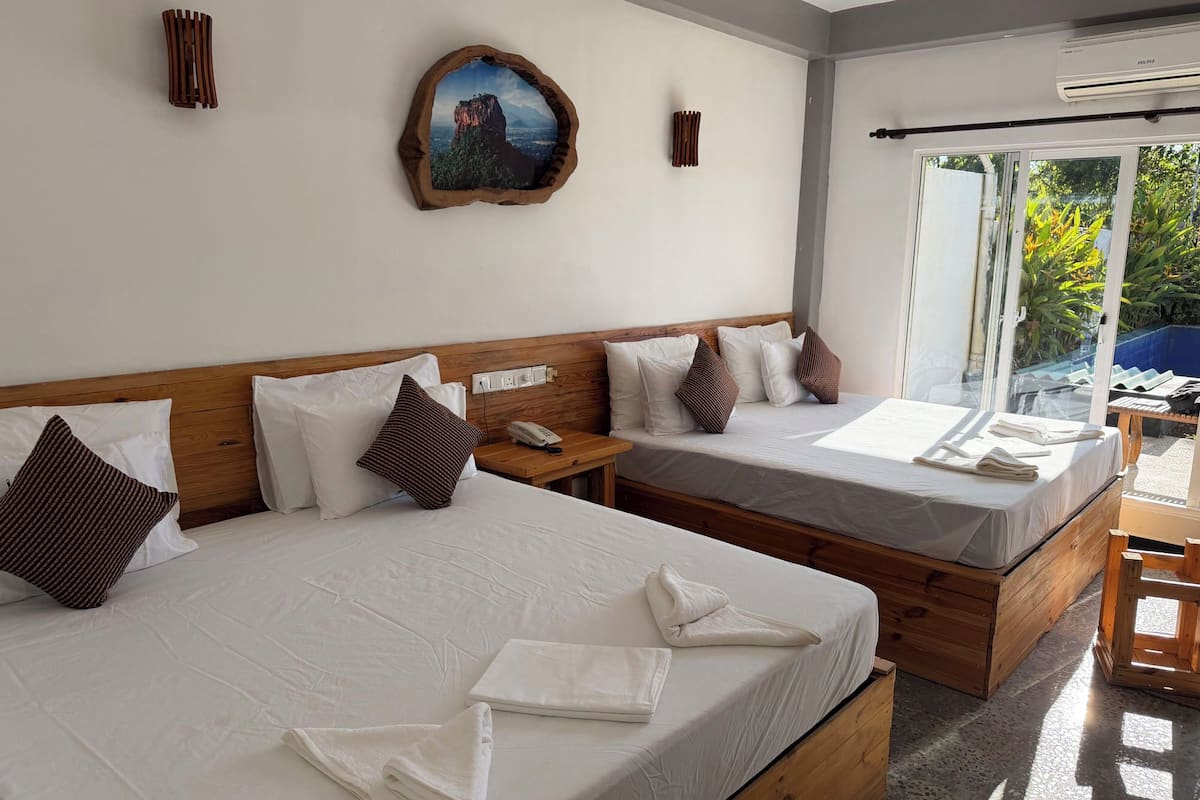 A hotel room with two beds, a wooden headboard, a painting on the wall, and a view of greenery through the window.