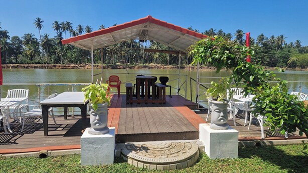 Un espacio al aire libre cubierto con mesas y sillas, rodeado de agua y palmeras.