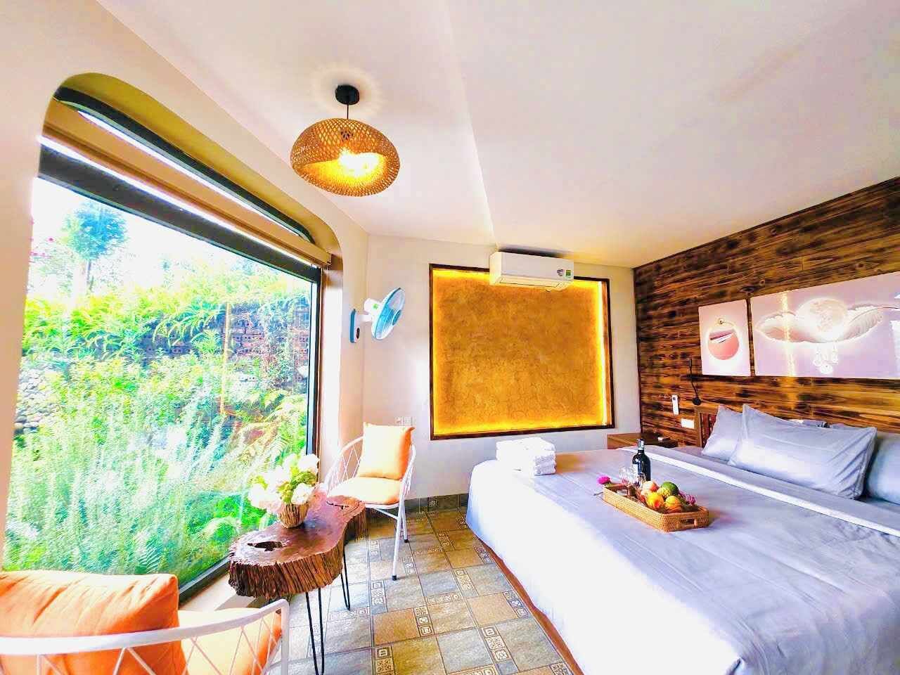 Ein modernes Schlafzimmer mit einem großen Bett, einem kleinen Tisch mit Blumen, einem Sessel und Blick ins Grüne.