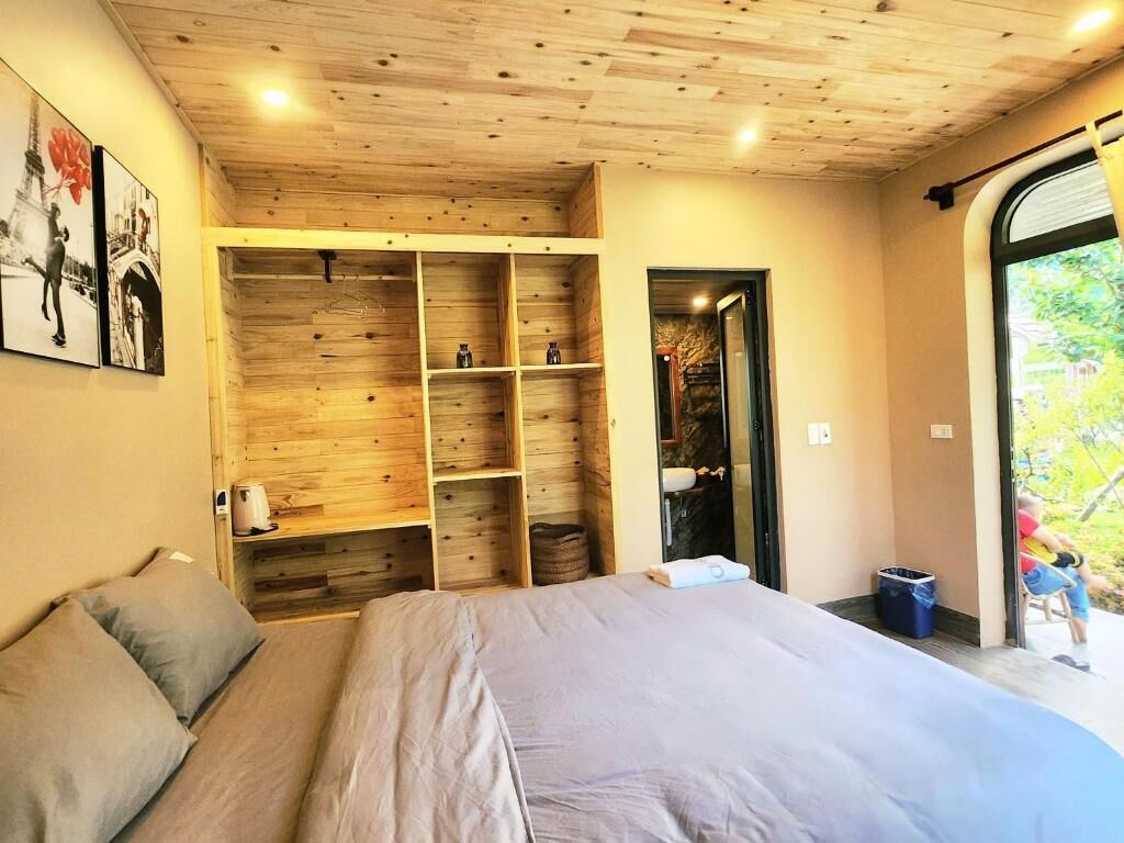 Ein Schlafzimmer mit einem großen Bett, Holzregalen und Blick durch eine Glastür.
