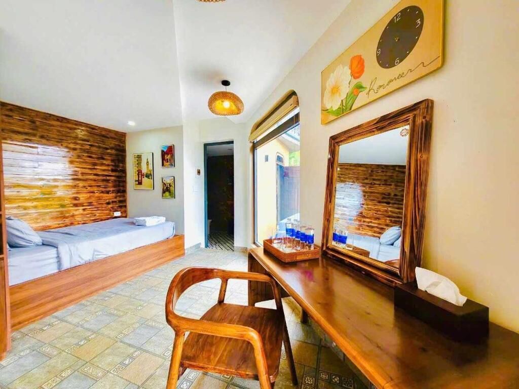 Quarto de hotel com cabeceira de madeira, uma cama, escrivaninha de madeira com espelho e uma cadeira.