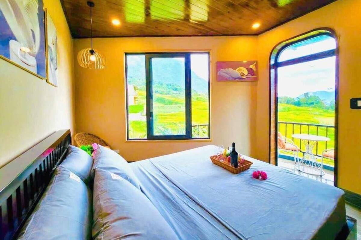 A bedroom with a bed, a window, and a balcony with a view of the countryside.