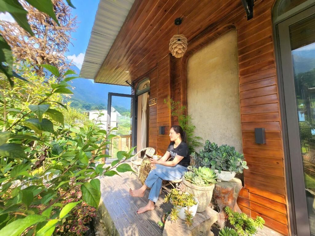 Une personne est assise sur un banc en bois, à l’extérieur d’un bâtiment dont la façade est en bois et qui possède de grandes fenêtres.
