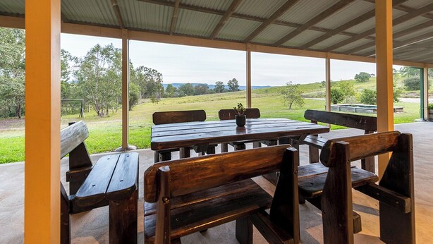 A covered outdoor seating area with wooden benches and tables, overlooking a grassy landscape. - Entire Home in Quorrobolong, lots of space, beautiful country, lots of wildlife (Quorrobolong)