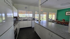 A modern kitchen with white cabinets, a granite countertop, and a view of the outdoors through large windows. - Entire Home in Quorrobolong, lots of space, beautiful country, lots of wildlife (Quorrobolong)