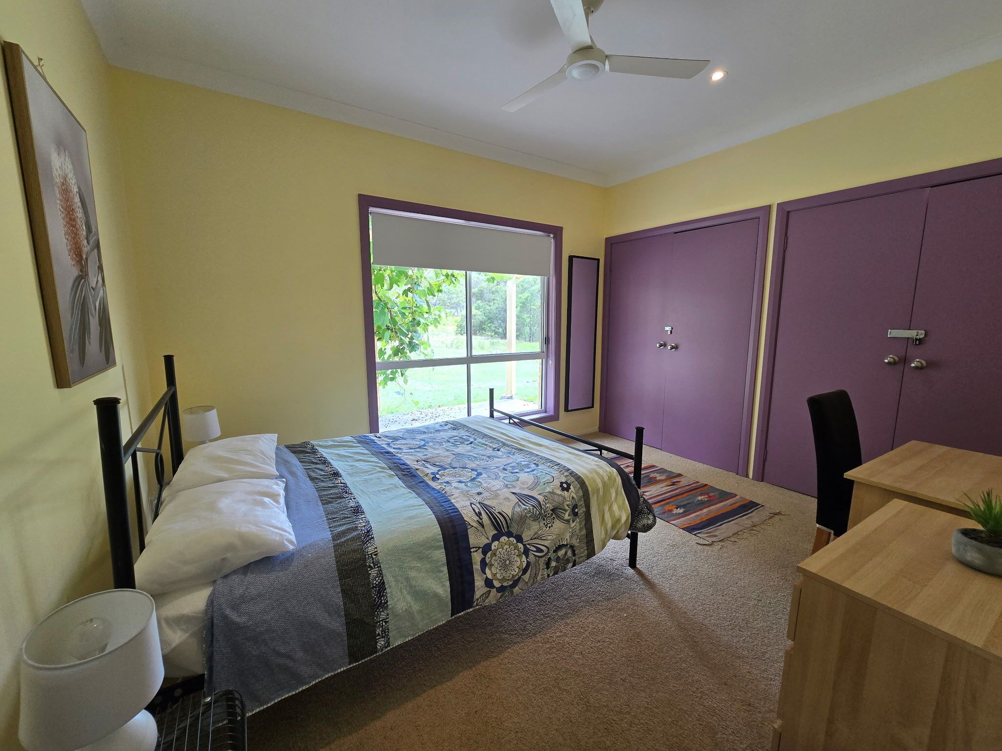 A bedroom with a bed, a desk, a chair, a window, and a ceiling fan.