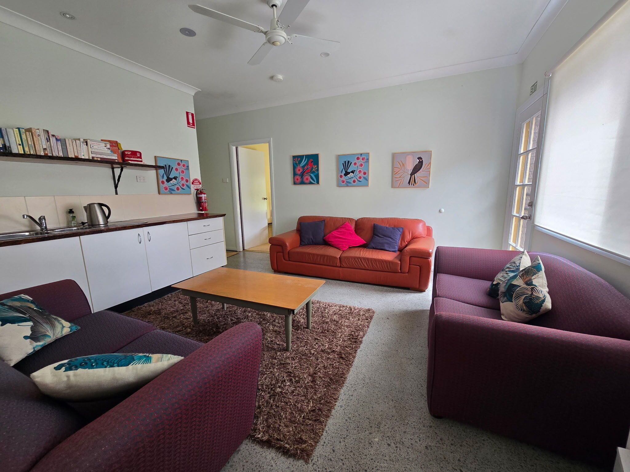 A living room with a sofa, a coffee table, and a couch. There is a kitchen area with a sink and a stove.
