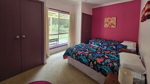 A bedroom with a bed, a ceiling fan, a window with curtains, a door, and a wall with a floral painting. - Entire Home in Quorrobolong, lots of space, beautiful country, lots of wildlife (Quorrobolong)