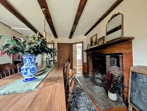 A dining room with a long wooden table, chairs, a blue vase with plants, a fireplace, and a wooden ceiling. - Luxury Coastal, Fire Pit, 5 minutes to the Beach (Surry)