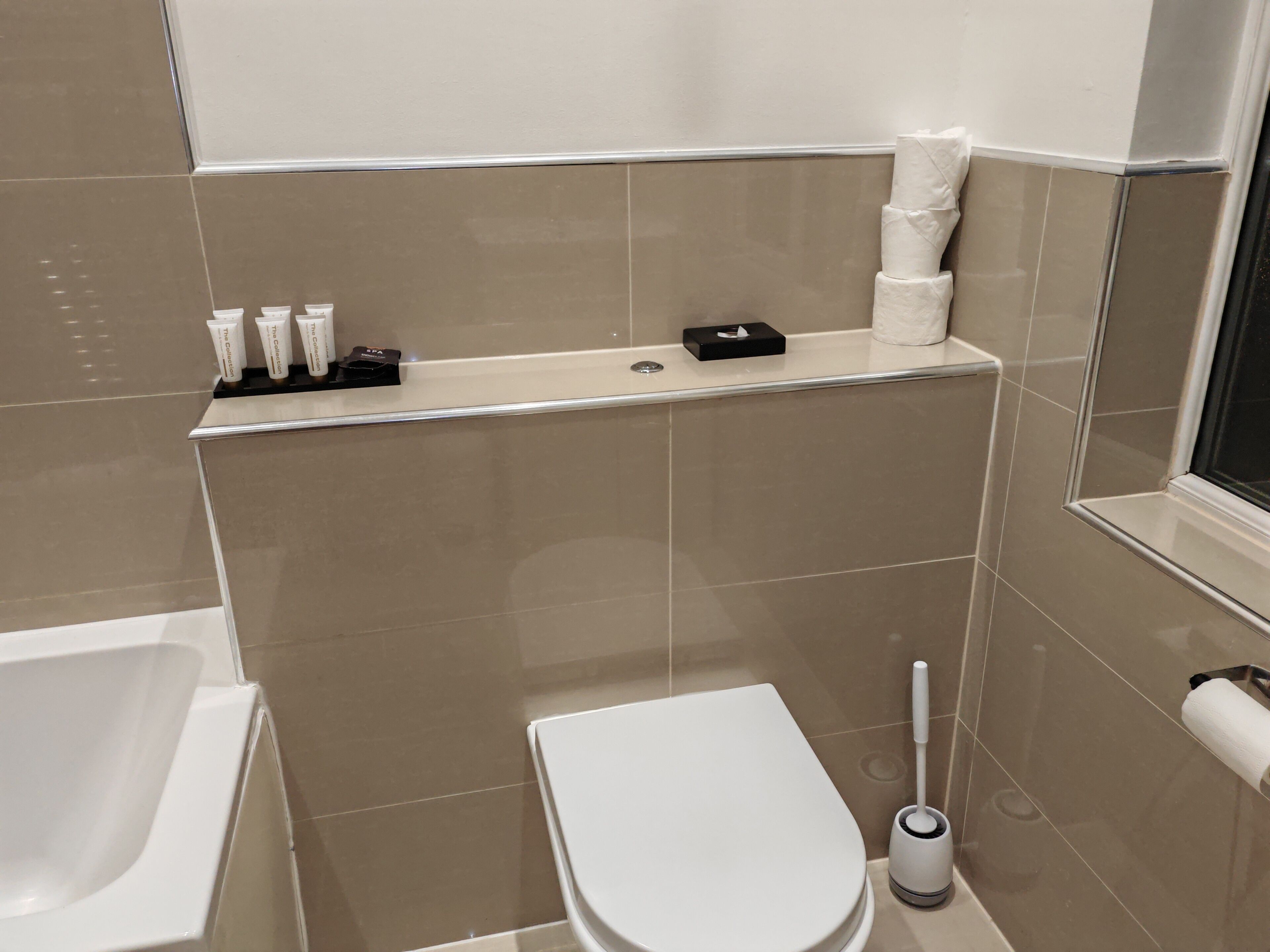 A small bathroom with a toilet, a bidet, and a shelf with toiletries.
