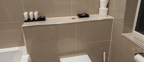 A small bathroom with a toilet, a bidet, and a shelf with toiletries.