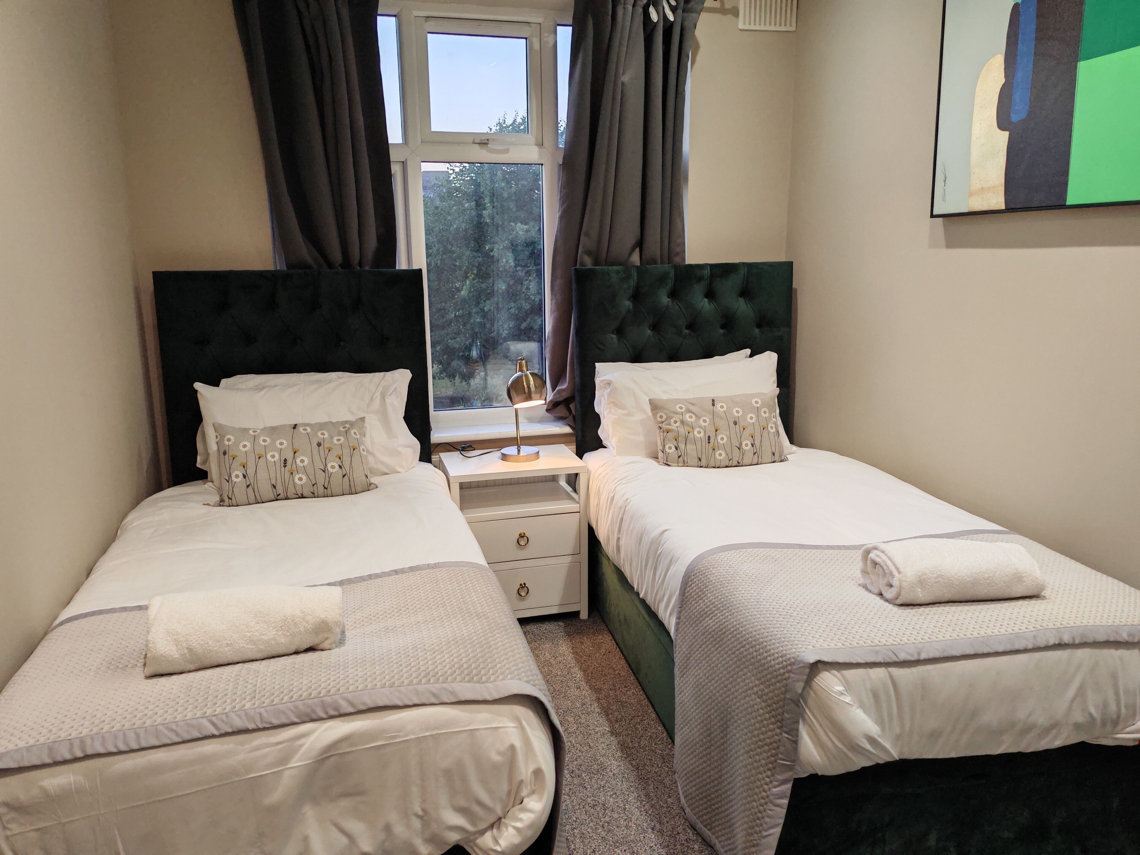 A twin room with two beds, a nightstand, a lamp, and a window with curtains.