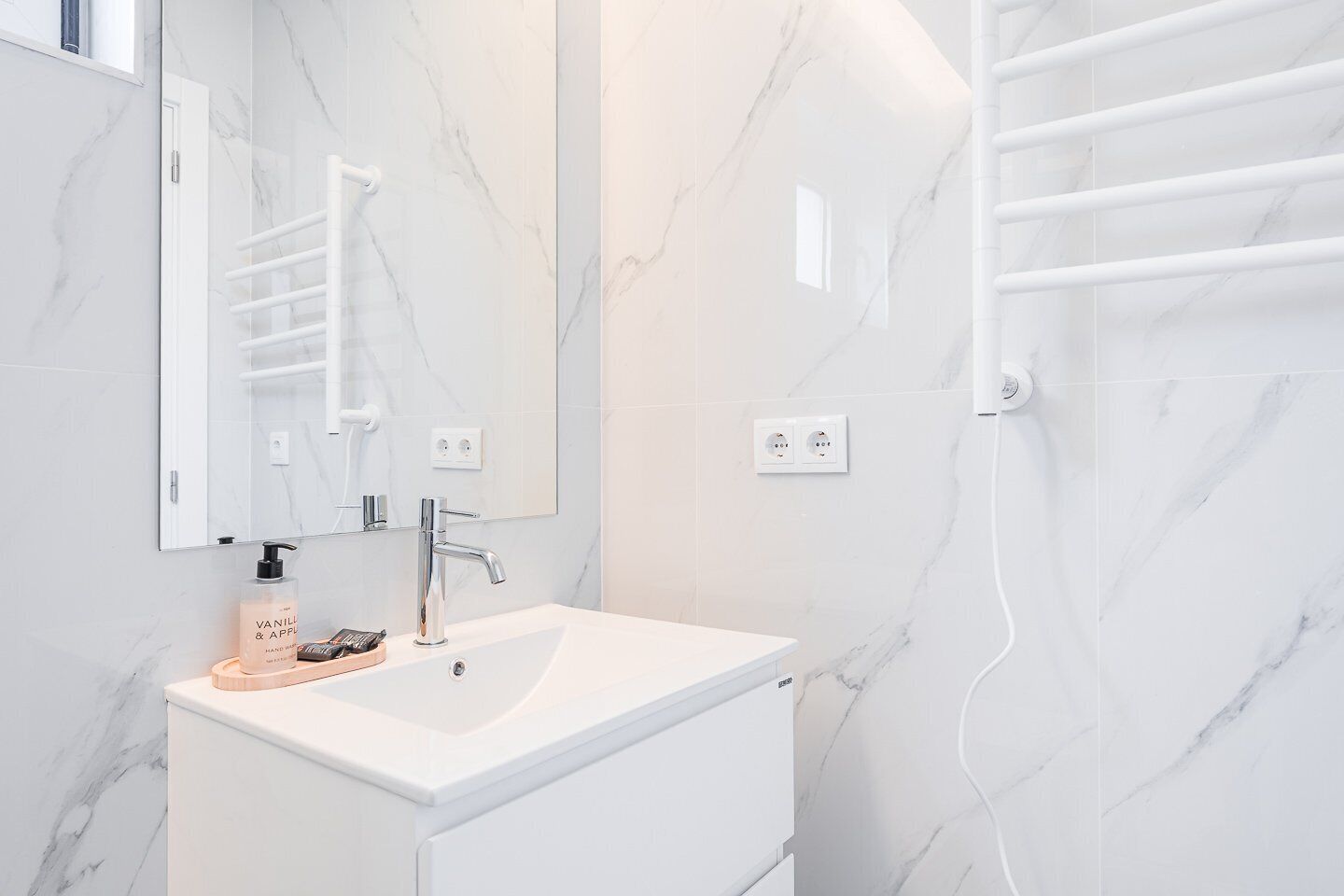 A modern bathroom with a white marble sink, a large mirror, and a towel rack.