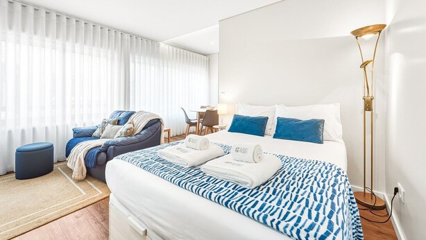 Ein modernes Hotelzimmer mit einem großen Bett, einer Sitzecke mit Sofa und Sesseln, einem kleinen Tisch und einer Stehlampe.