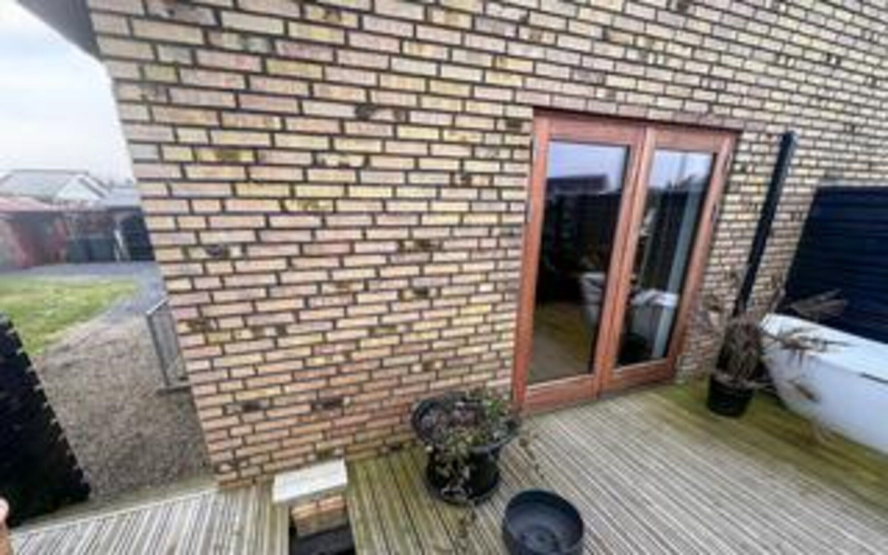 A brick exterior wall, a sliding glass door, and a potted plant on a wooden deck.