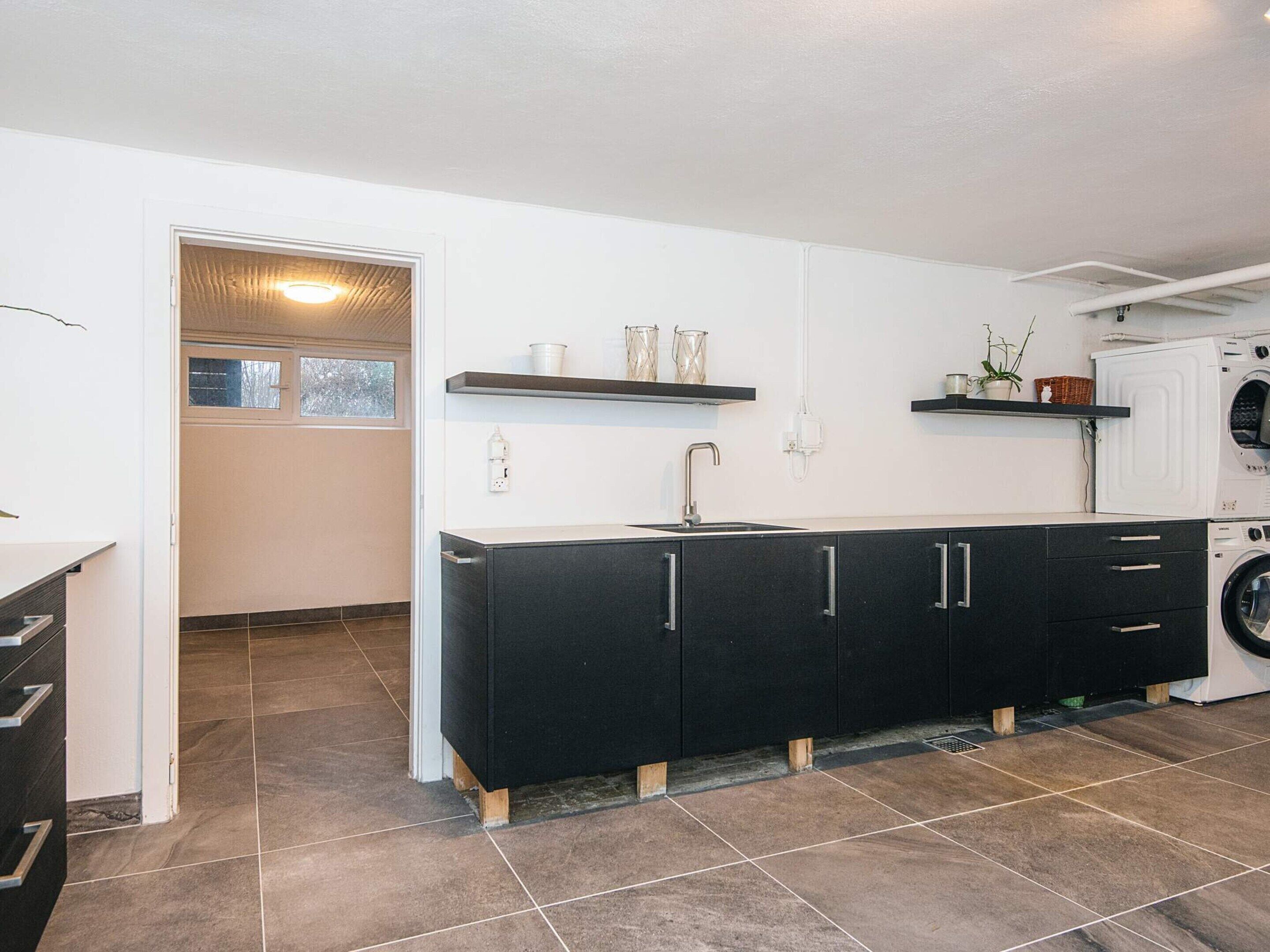A modern kitchen with a black cabinet, a built-in washing machine, and a window with a view.
