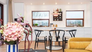 A modern living room with a yellow sofa, a dining table with four chairs, and a kitchen area with two windows and a shelf with various items. - 4 Star Holiday Home in Viborg (Viborg)