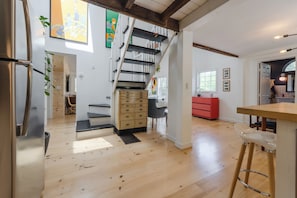 Eine geräumige Küche mit Holzboden, einem Edelstahlkühlschrank, einer Treppe mit schwarzer Geländer und einem roten Schrank.
