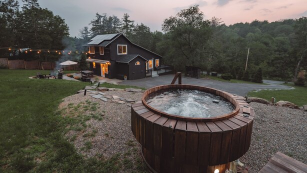 Una casa con jacuzzi en el jardín, rodeada por una terraza de madera y un sendero de piedra.