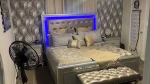 Quarto com cama, mesa de cabeceira, ventilador e ventoinha no teto.