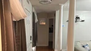 Um corredor com piso de madeira, colunas brancas e um candelabro.