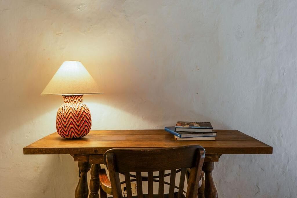 A wooden table with a patterned lamp, a chair, and a stack of books.
