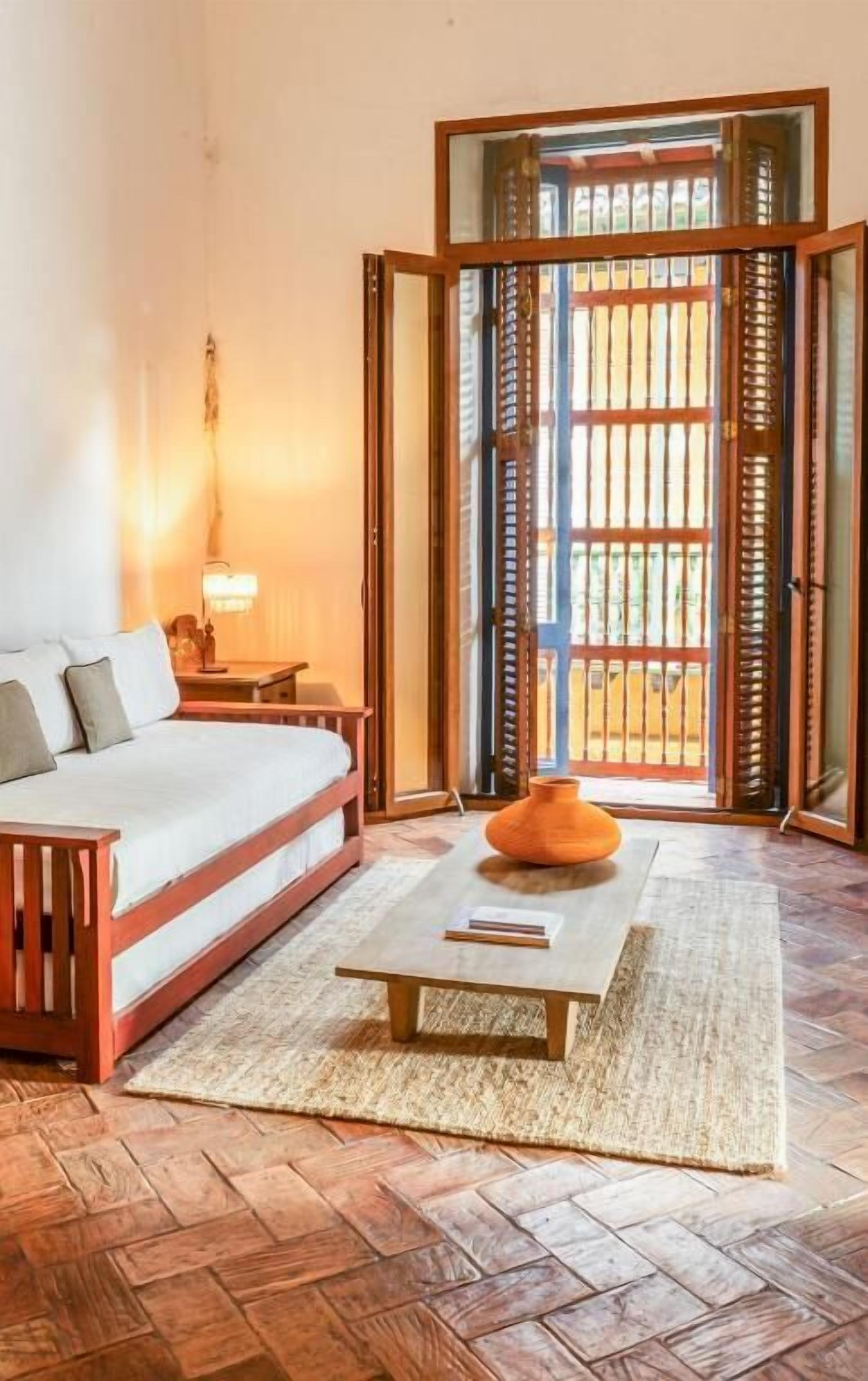 A bedroom with a bed, a nightstand, a lamp, a coffee table, and a view through a sliding door.