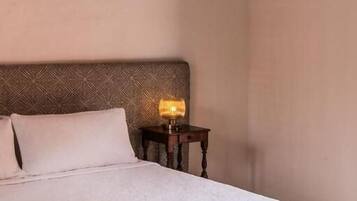 A neatly made bed with a white duvet, a wooden bench with a yellow throw, and a nightstand with a lamp.