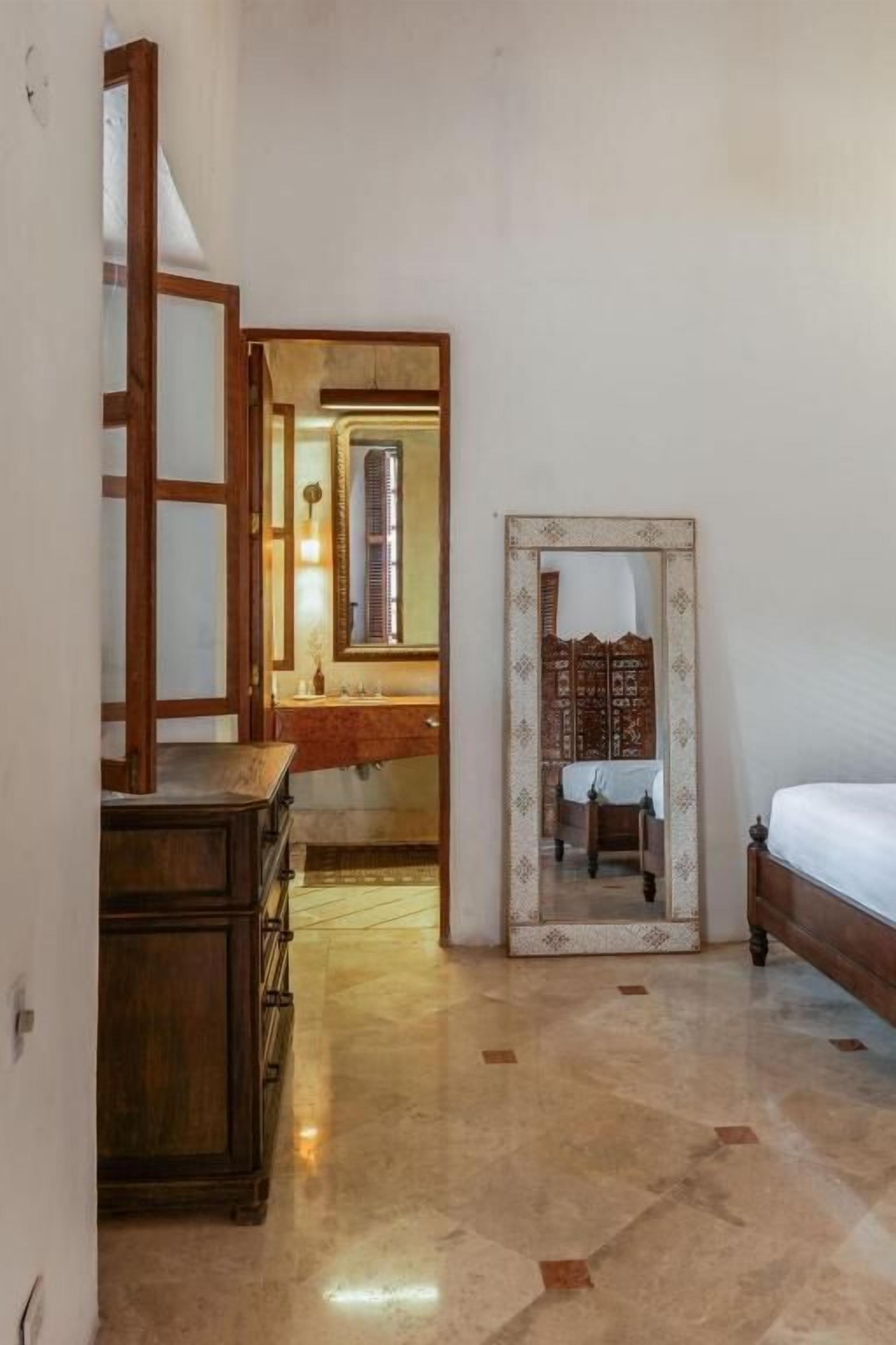 A room with a wooden dresser, a bed with a white mattress, and a mirror with a decorative frame.