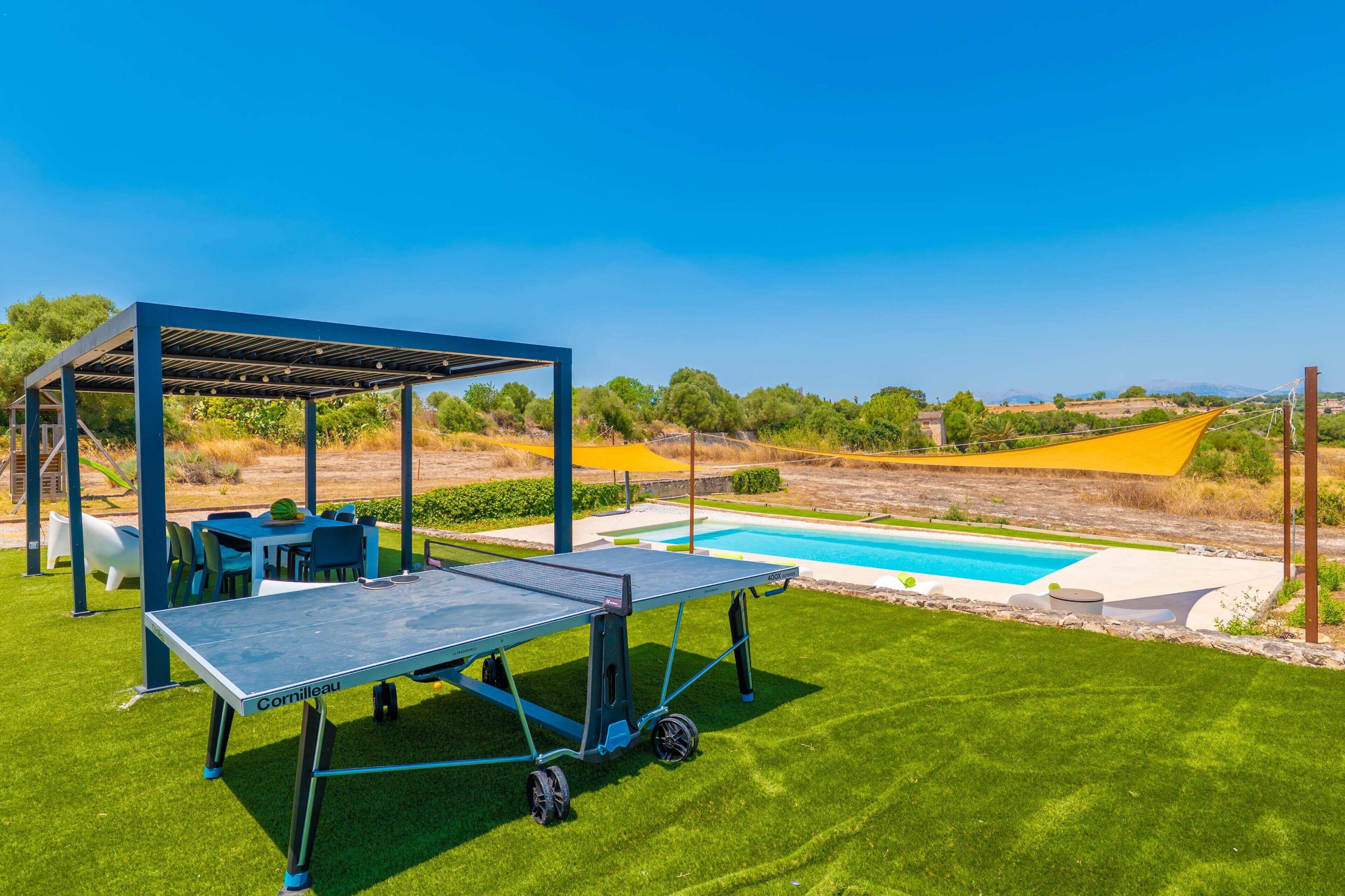 A pool table with a canopy, outdoor seating, and a view of a swimming pool and landscape.
