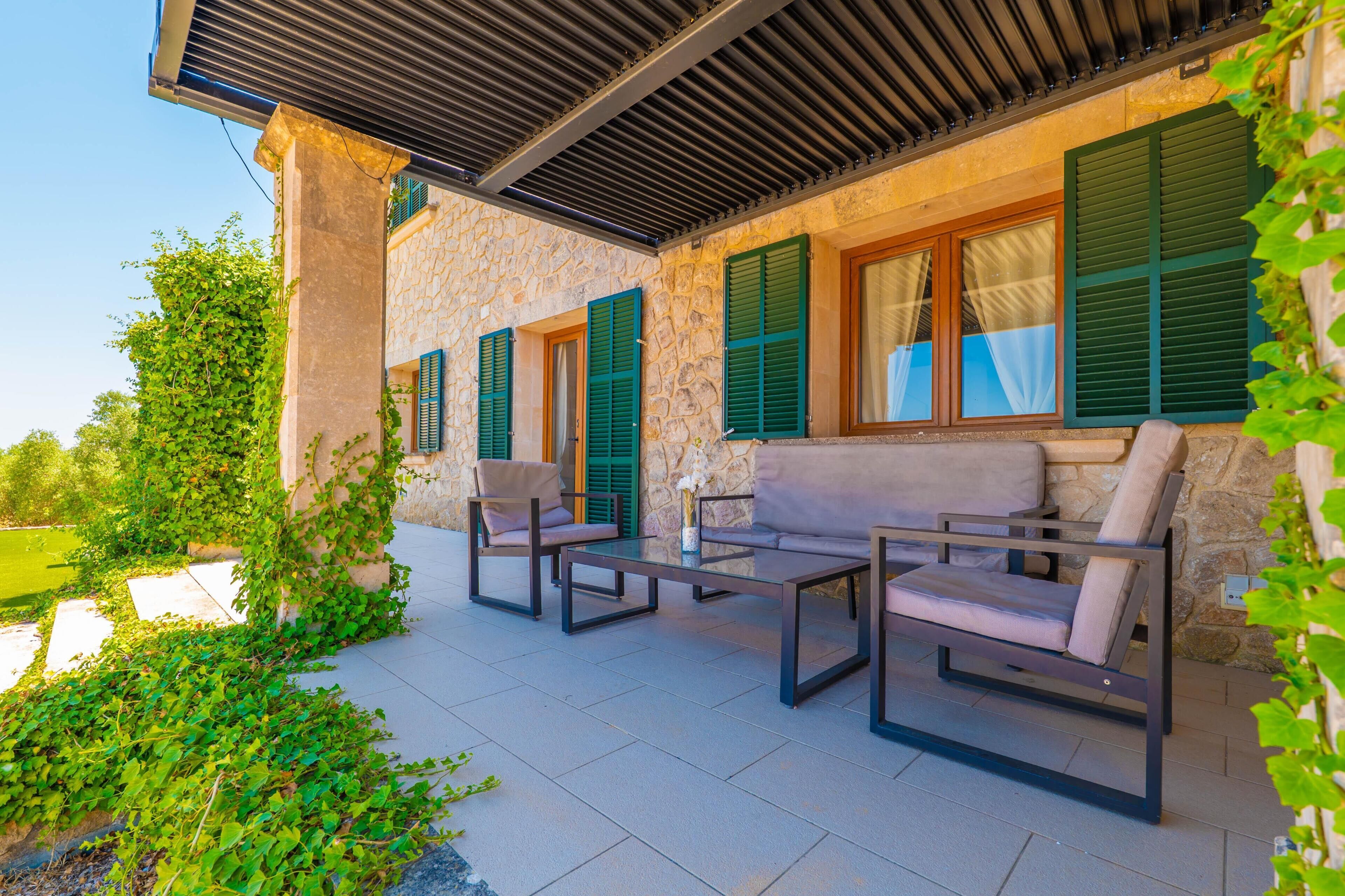 Un espace extérieur aménagé en terrasse, avec des murs en pierre, des volets verts et du mobilier d’extérieur.